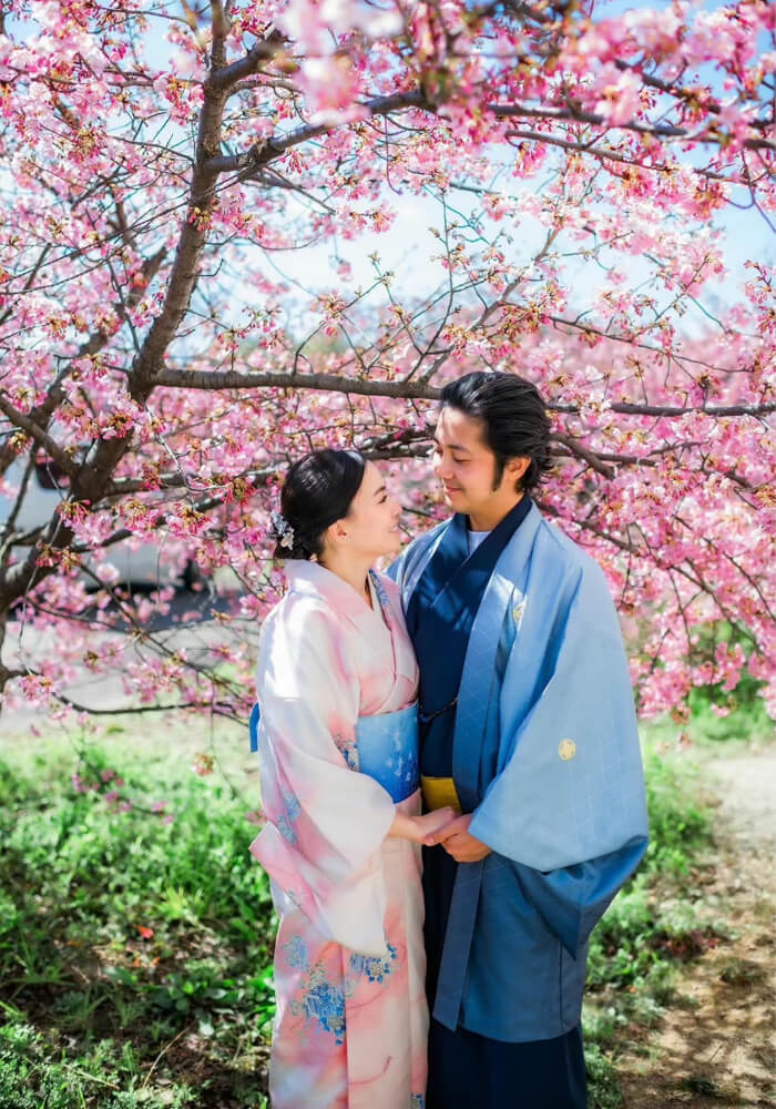 Couple in matching seasonal kimono walking hand in hand along the Shirakawa Canal in Gion, autumn leaves reflected in water